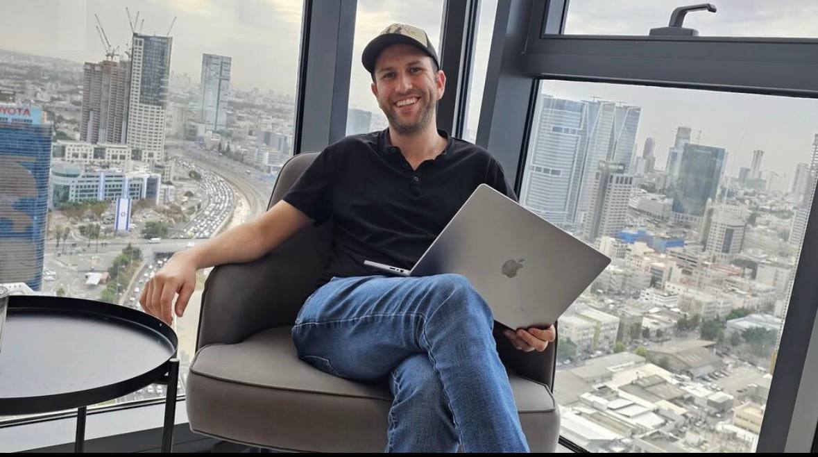 אלכס עם מחשב נייד מול קו הרקיע של העיר